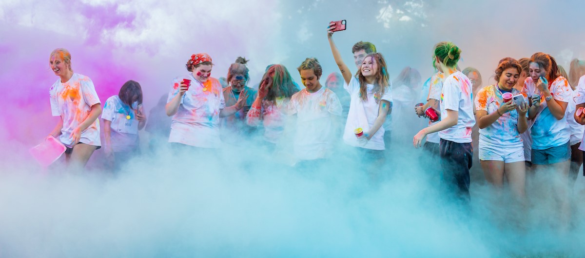 Group of students wearing tie-dyed shirts celebrating the start of school with color powder.