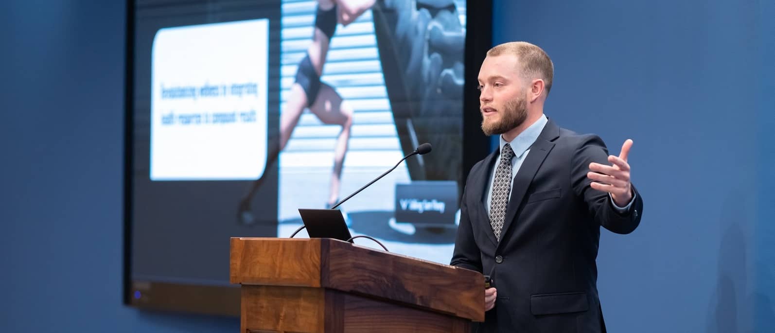 Student in business attire standing at the podium, presenting his proposal to the audience.