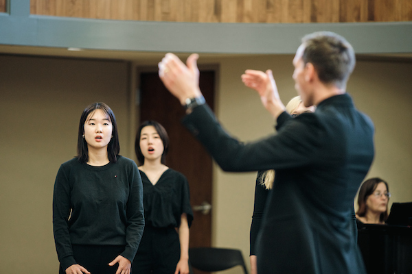 Several students and the choir leader, all dressed in black, rehearsing for the annual showcase.