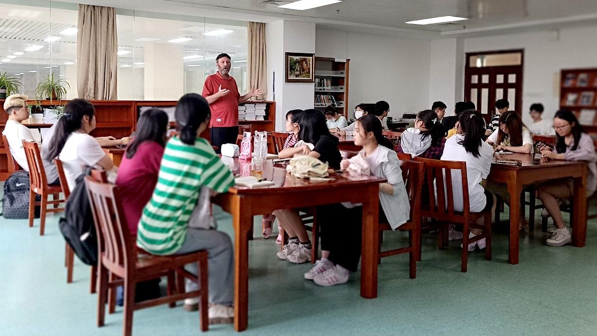 Classroom full of students, focusing on person standing leading the discussion.