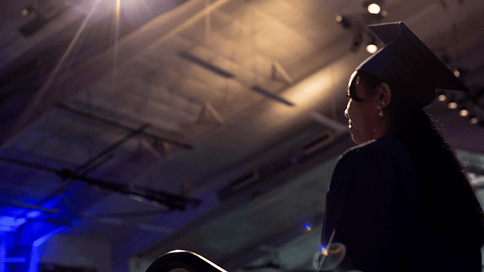 Side view of a proud graduate looking toward the stage under the spotlights of the commencement ceremony.