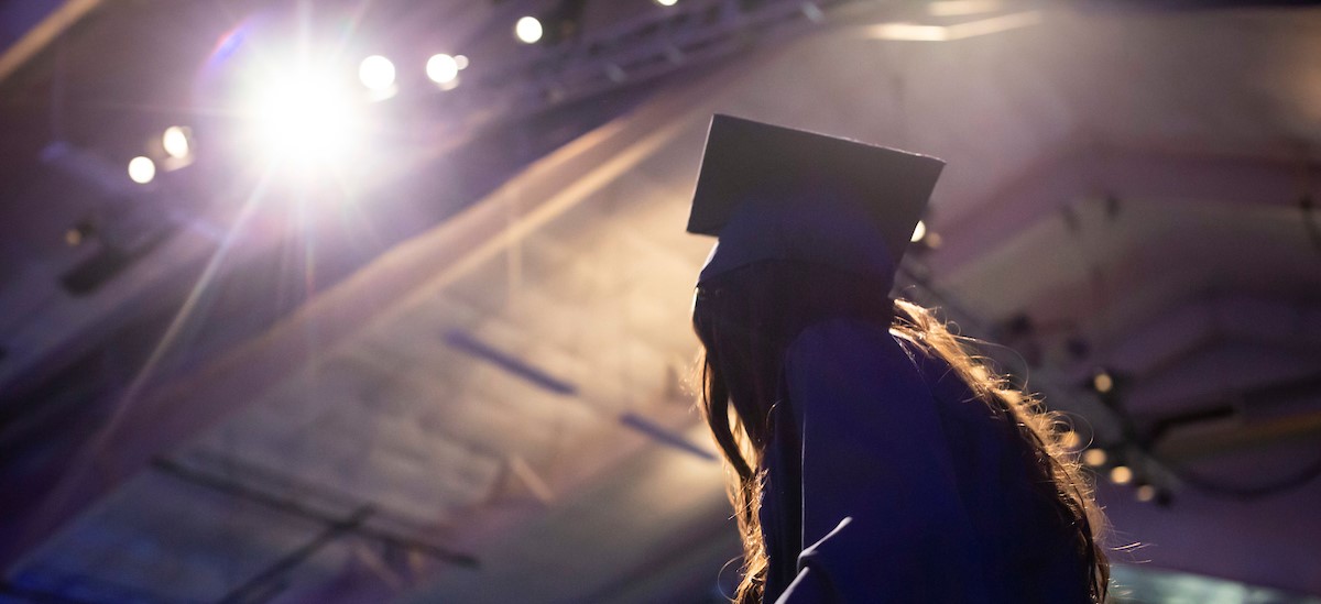 Side view of a proud graduate looking toward the stage under the spotlights of the commencement ceremony.