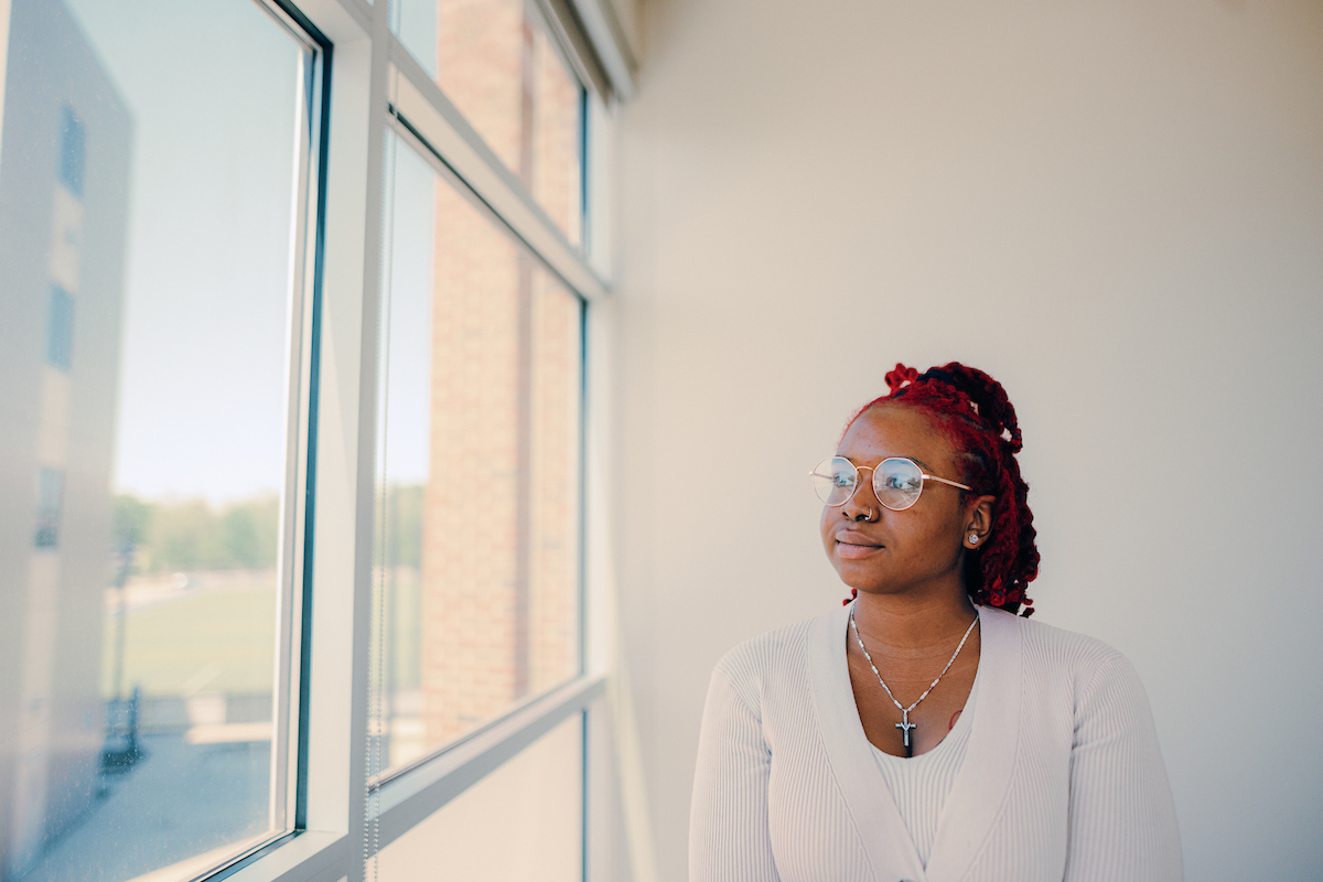 Business professional standing near a bank of windows, glancing out to her right.