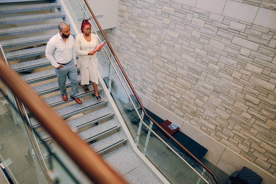 Two adult students, one holding a folder, talking as they walk down the stairs.