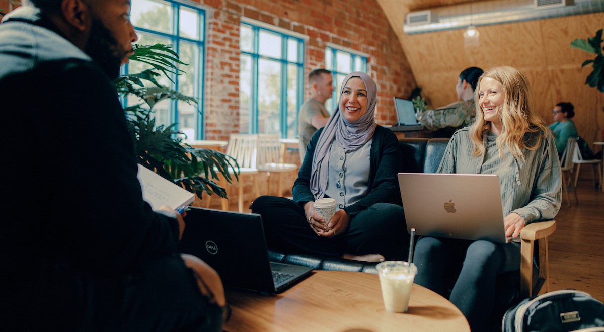 Students sitting around a coffee shop with their laptops and coffee mugs, smiling.