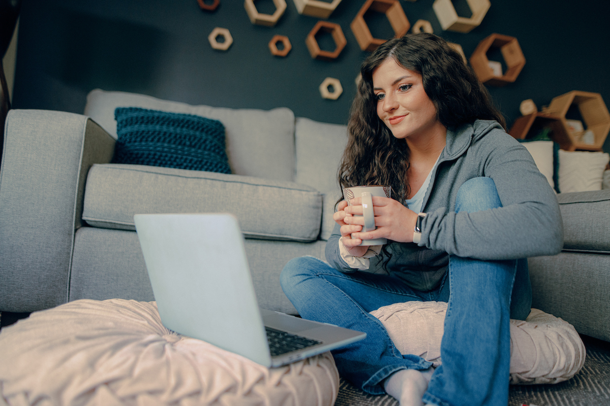 Course Schedule: Student seated on a couch holding a coffee mug while looking at a laptop.