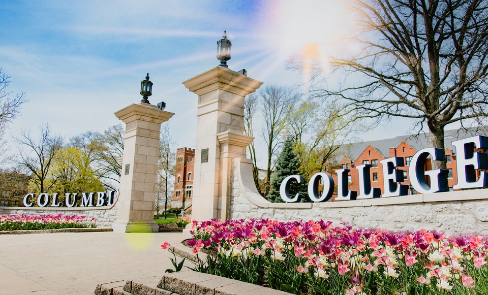 Rogers Gate entrance into Columbia College in the spring, surrounded by colorful blooming flowers.