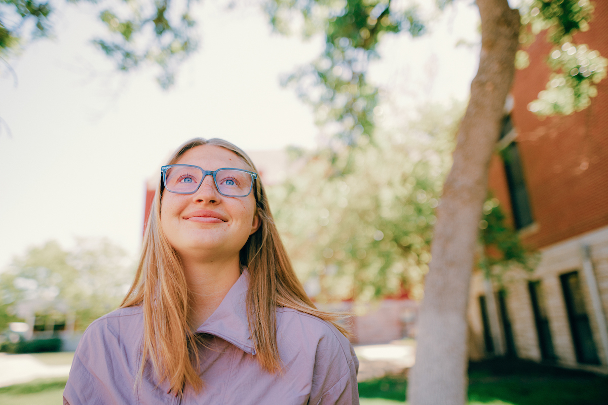 Woman with long blonde hair and wearing glasses staring up at the sky.