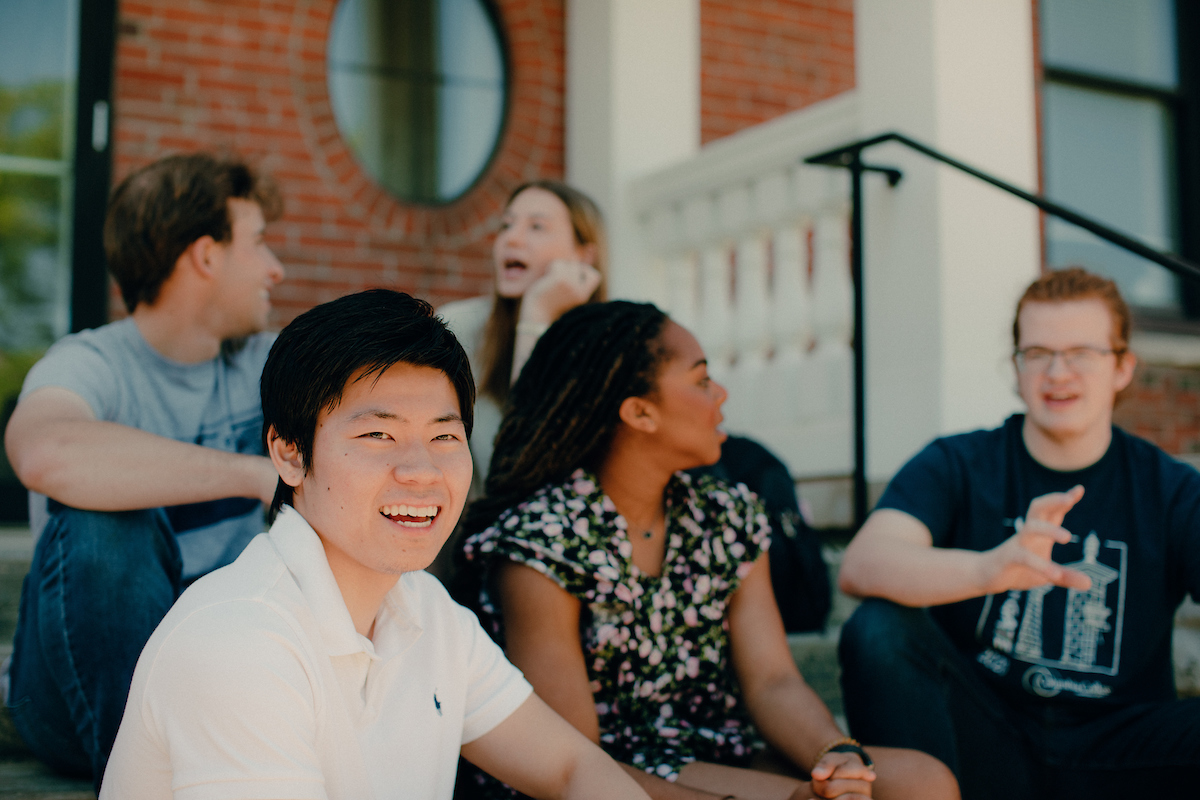 Several students sitting on the steps outside a campus building.