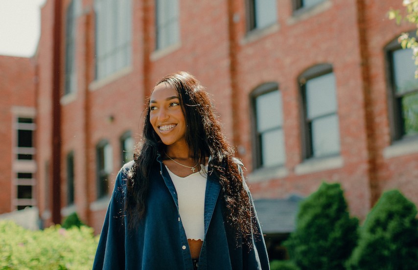 For International Students: Woman smiling while standing outside and looking up, off to her right.