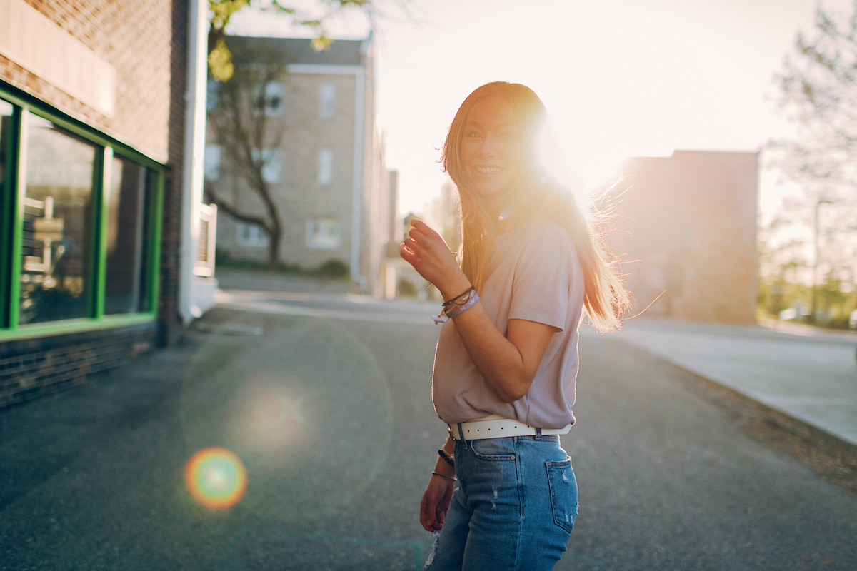 Columbia College student walking downtown Columbia, MO, turning to smile at the camera with the sun shining behind her.