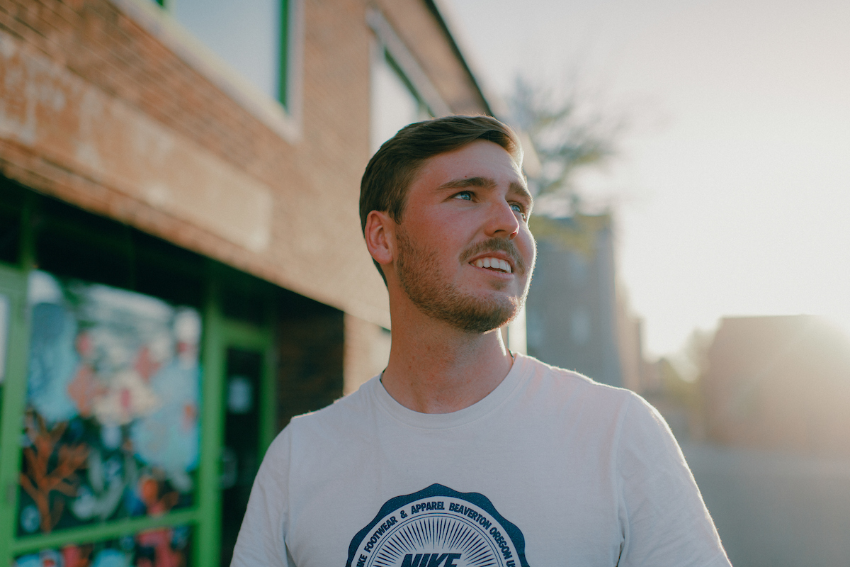 Student walking past shops in downtown Columbia, MO, while have a conversation with someone to his left.