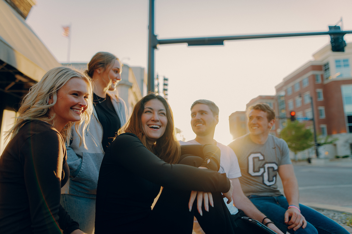 Group of students, one wearing a "CC" t-shirt, sitting on a bench in downtown Columbia, MO.