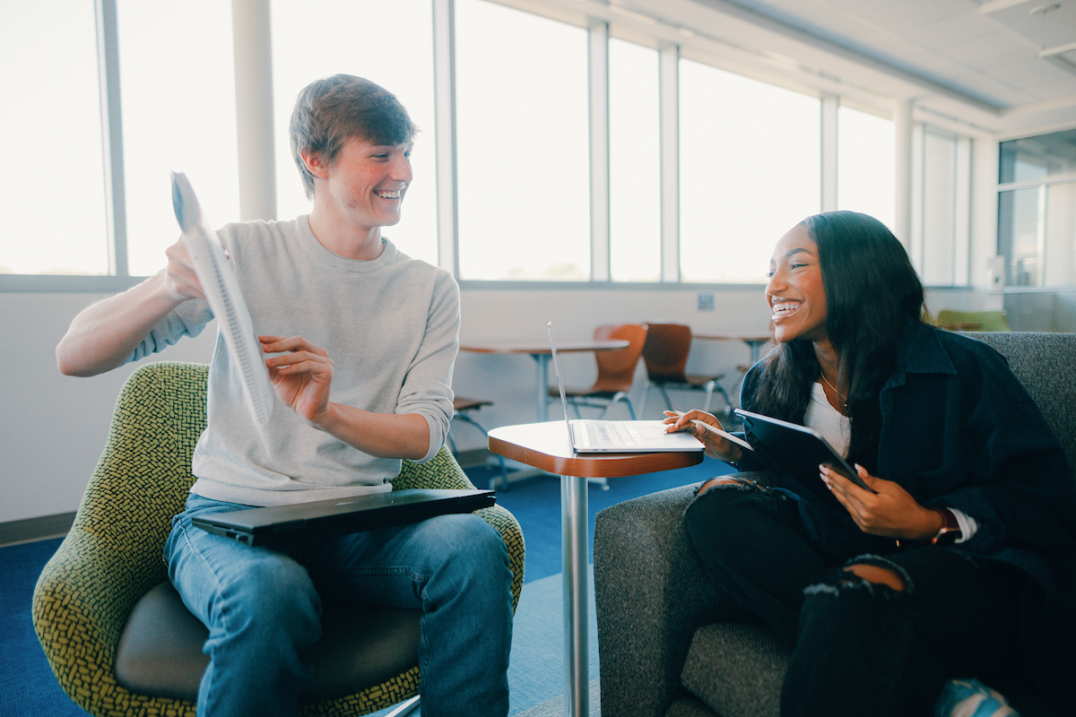 Syllabi: Two students sitting around a table working on a project together.