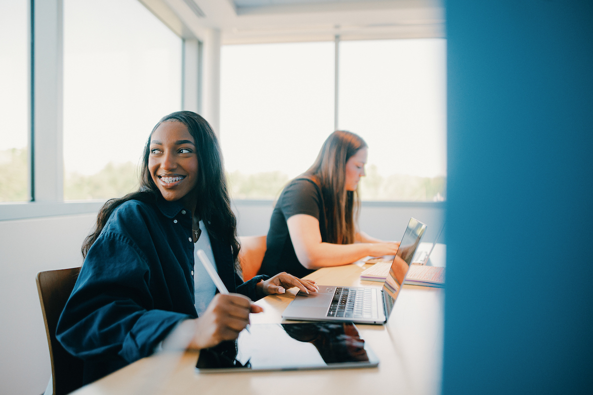 Two women, sitting at a table, working with laptops in their coursework toward a Bachelor of Science in History degree.