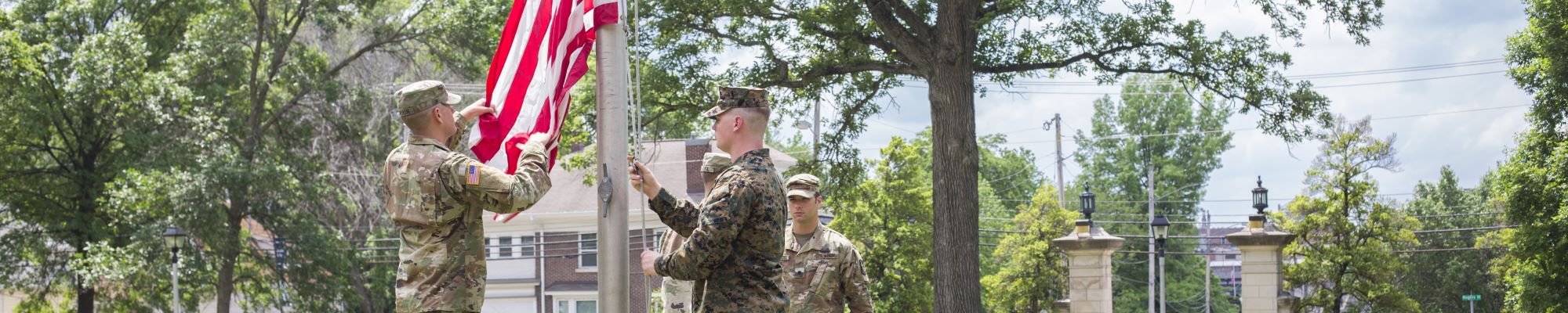 Two men dressed in military uniform raising the American flag.