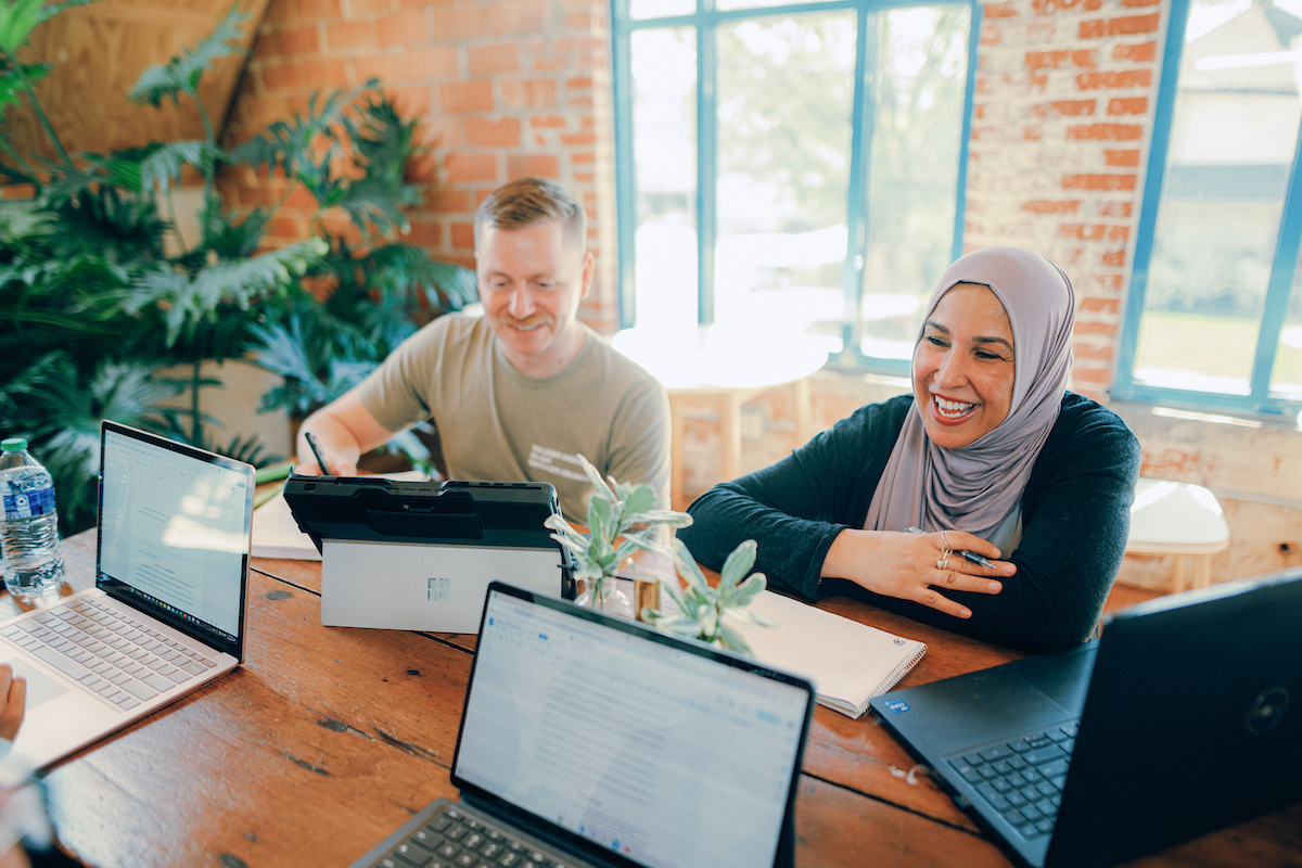 Course Schedule: Two students working together while sitting at a table, surrounded by laptops and notebooks.