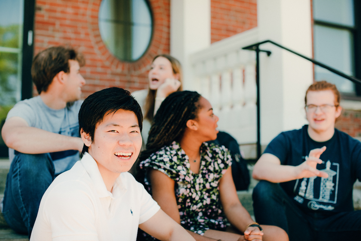 Academic Calendar: Several students sitting on stairs in front of a building, engaged in conversation.