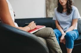 Counselor, seated and holding notepad and pencil, talking with student, also seated.