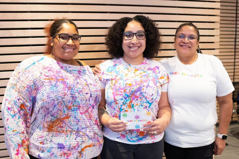 Three women showing off their business idea, Paint to Pieces, at the Student Pitch Competition.